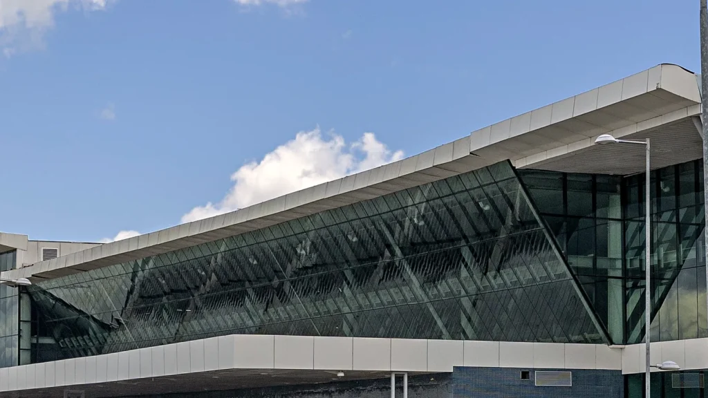 Fachada de vidro do terminal de passageiros do aeroporto de Manaus sob céu azul com nuvens