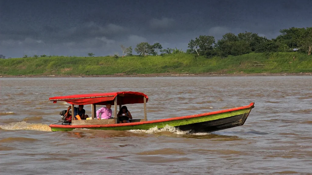 Canoa de passageiros com toldo vermelho navegando no rio Solimões perto de Tabatinga, com a margem verde e céu de chuva ao fundo