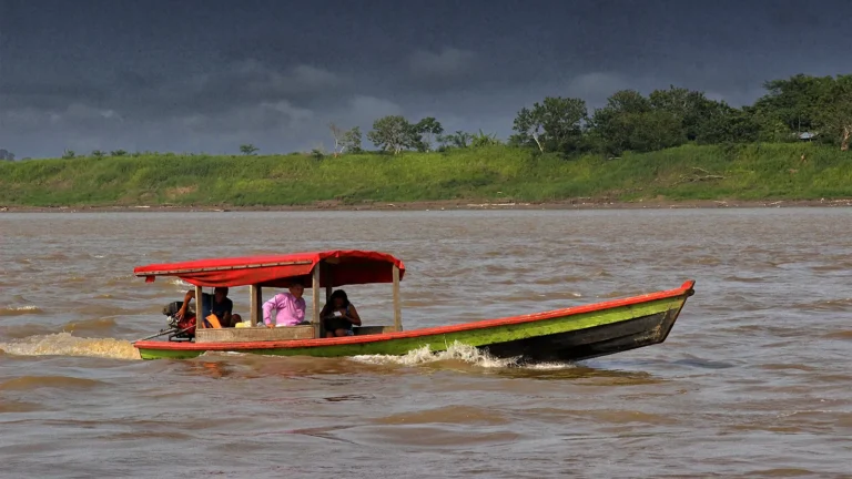 Canoa de passageiros com toldo vermelho navegando no rio Solimões perto de Tabatinga, com a margem verde e céu de chuva ao fundo