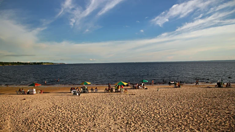 Praia da Ponta Negra com faixa larga de areia às margens do rio Negro, em Manaus, com guarda-sóis e céu azul em dia de sol