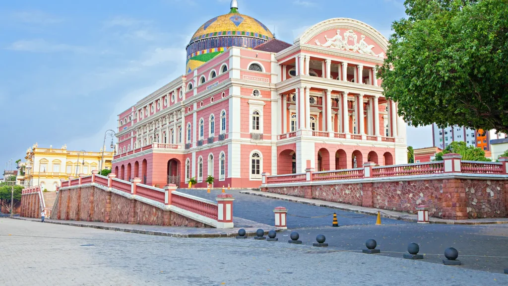 Fachada rosa do Teatro Amazonas com a cúpula colorida, vista do Largo de São Sebastião em Manaus num dia de céu claro
