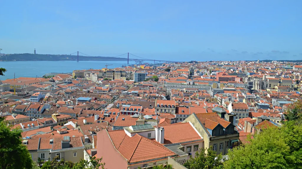 Vista de Lisboa a partir do Castelo de São Jorge, com telhados do centro, o rio Tejo e a ponte 25 de Abril em dia de sol