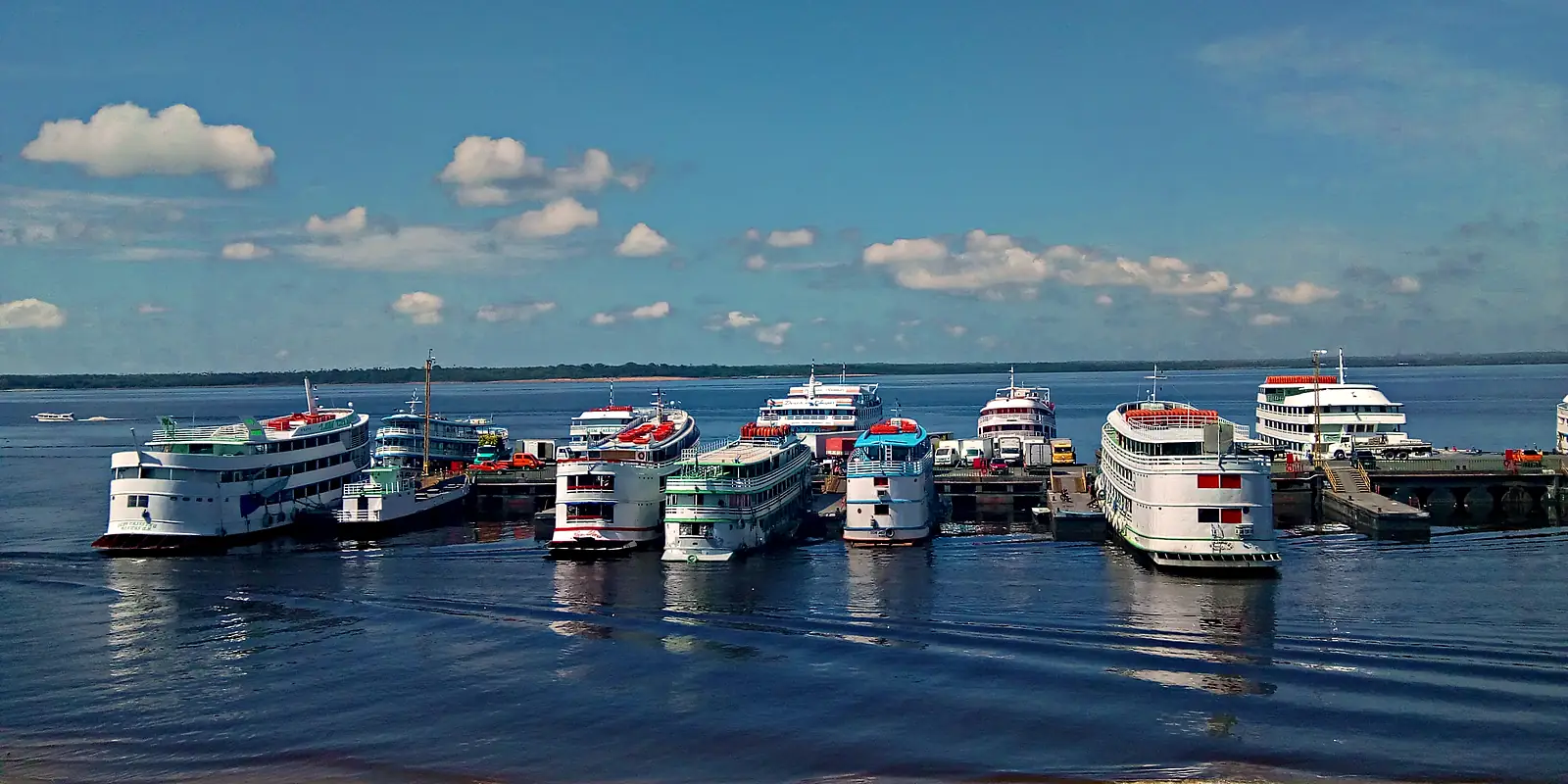 Barcos de recreio de três andares atracados lado a lado no cais do Porto de Manaus, no rio Negro, com caminhões no pátio